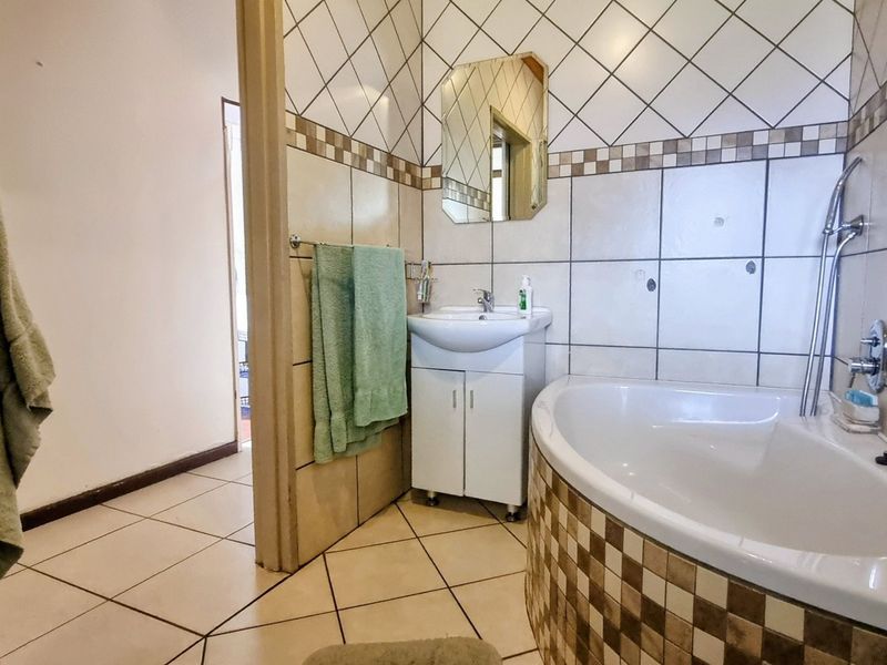 A functional bathroom featuring a corner bathtub, vanity basin, and decorative wall tiling, offering a practical layout with potential for modern updates.