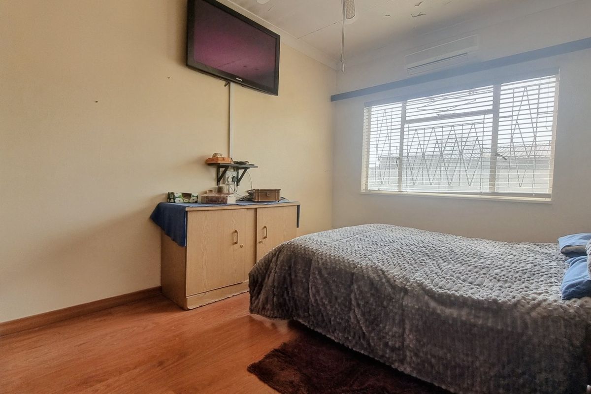A bedroom featuring laminate flooring, a wall-mounted air conditioner, and security bars on the window. The ceiling shows signs of wear and damage.