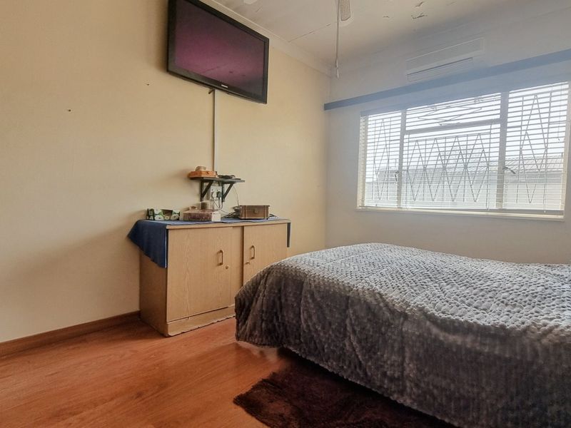 A bedroom featuring laminate flooring, a wall-mounted air conditioner, and security bars on the window. The ceiling shows signs of wear and damage.