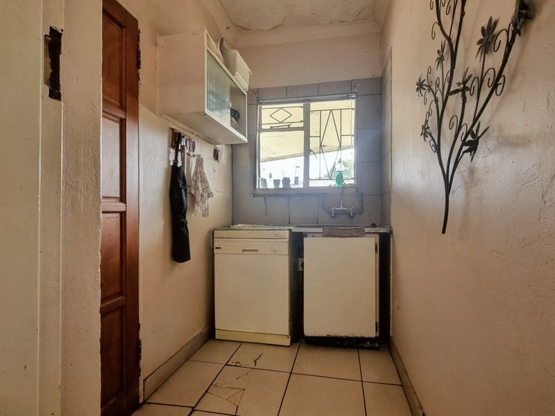 A compact laundry area featuring tiled flooring, built-in cabinetry, and a sink, currently showing signs of wear and requiring maintenance.