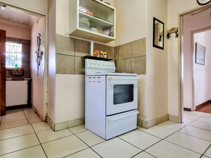 A dated kitchen area featuring a freestanding stove, tiled splashback, and ceramic floor tiles, with access to adjacent rooms.
