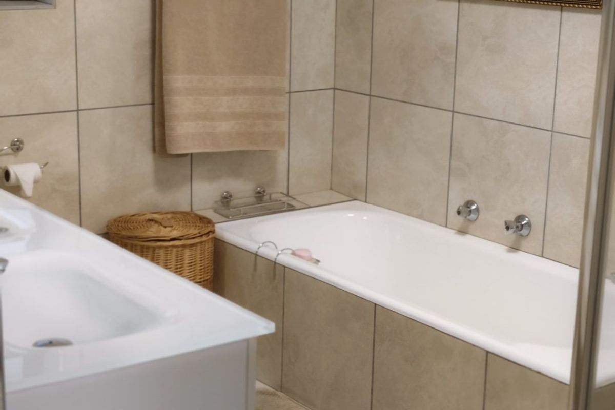A functional bathroom featuring a built-in bathtub, vanity basin, and neutral tiled finishes throughout.