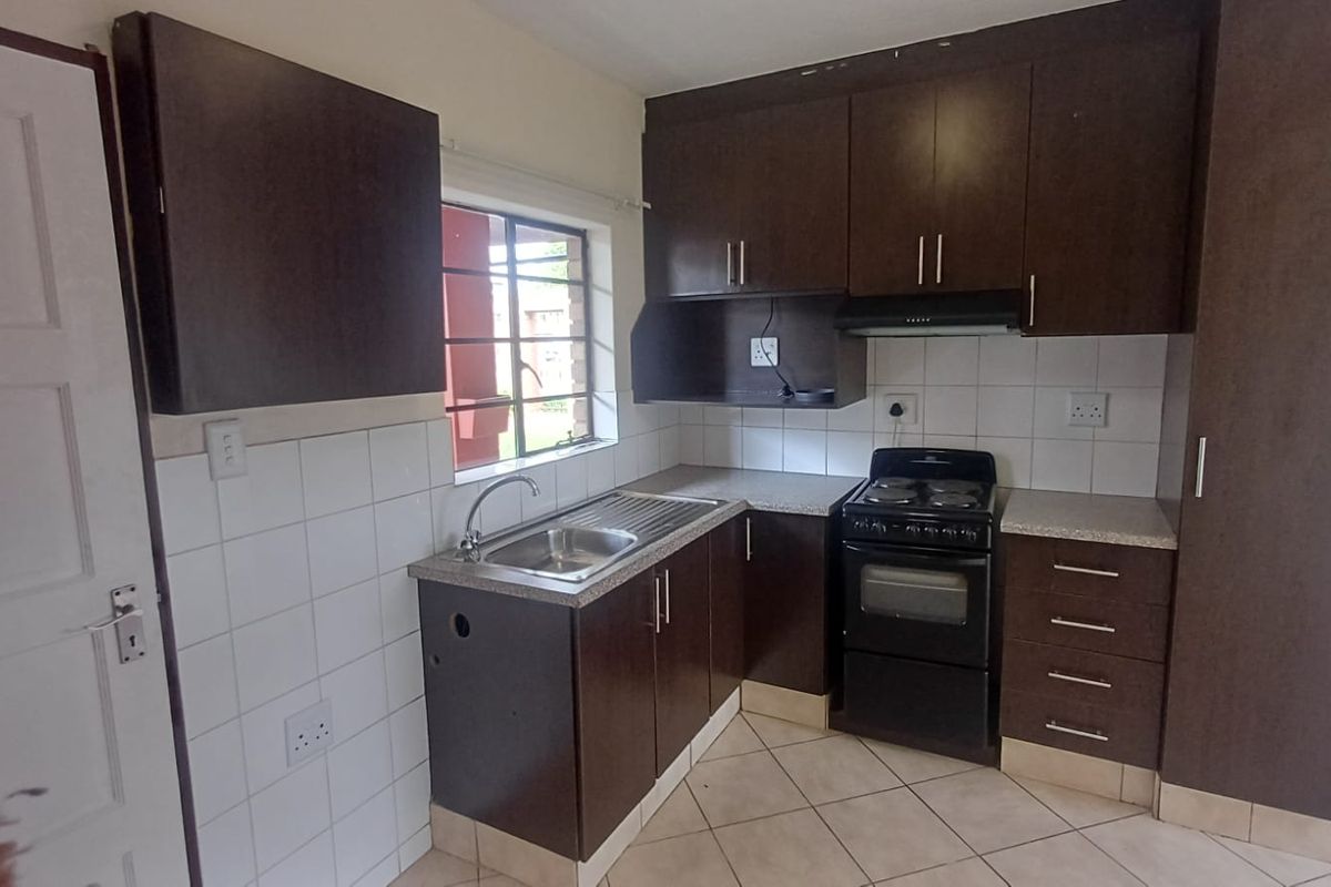 Compact kitchen featuring dark wood cabinetry, laminate countertops, tiled backsplash, and a freestanding stove. The space is functional but requires minor maintenance.