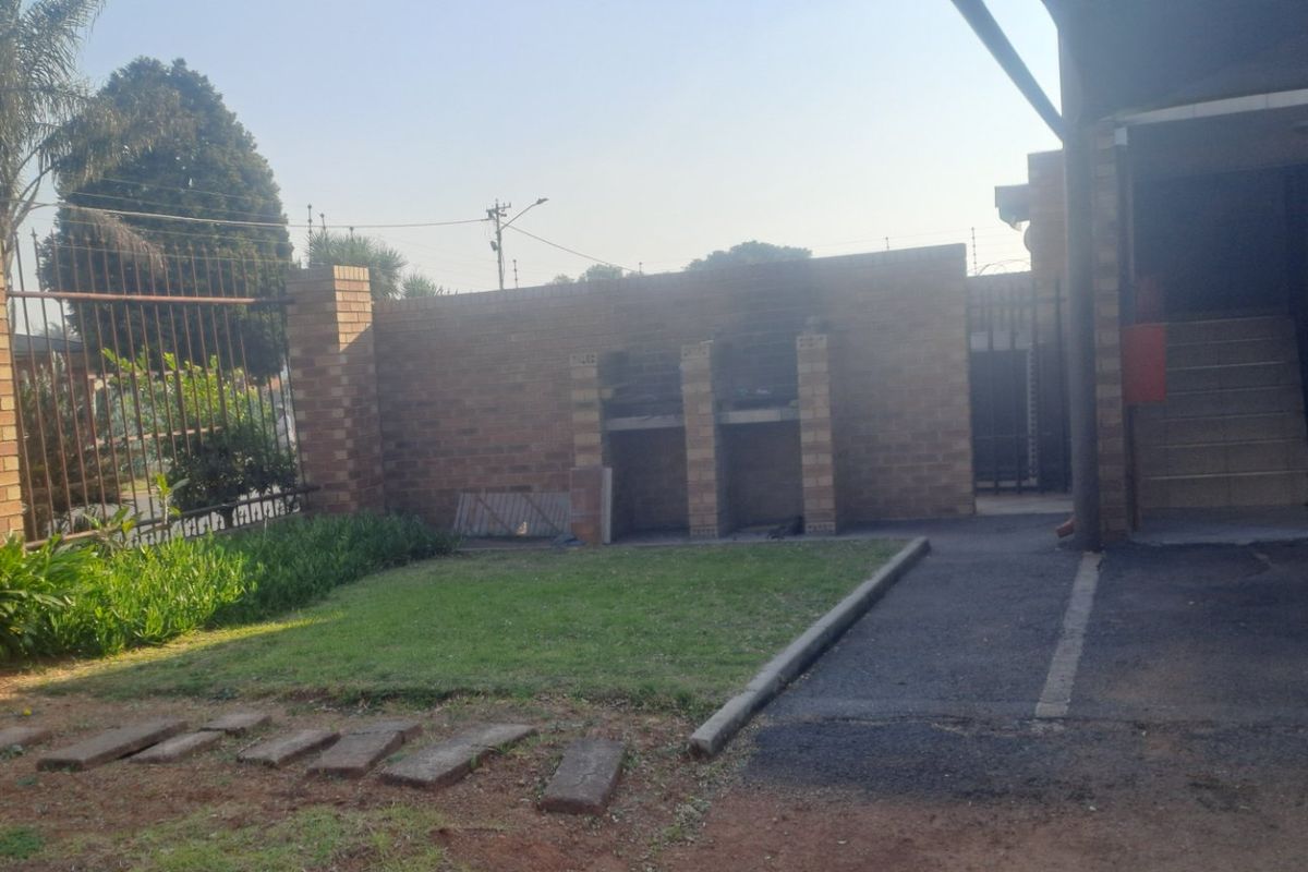Rear exterior area featuring a small lawn, built-in brick braai, paved driveway, and access to an external staircase.