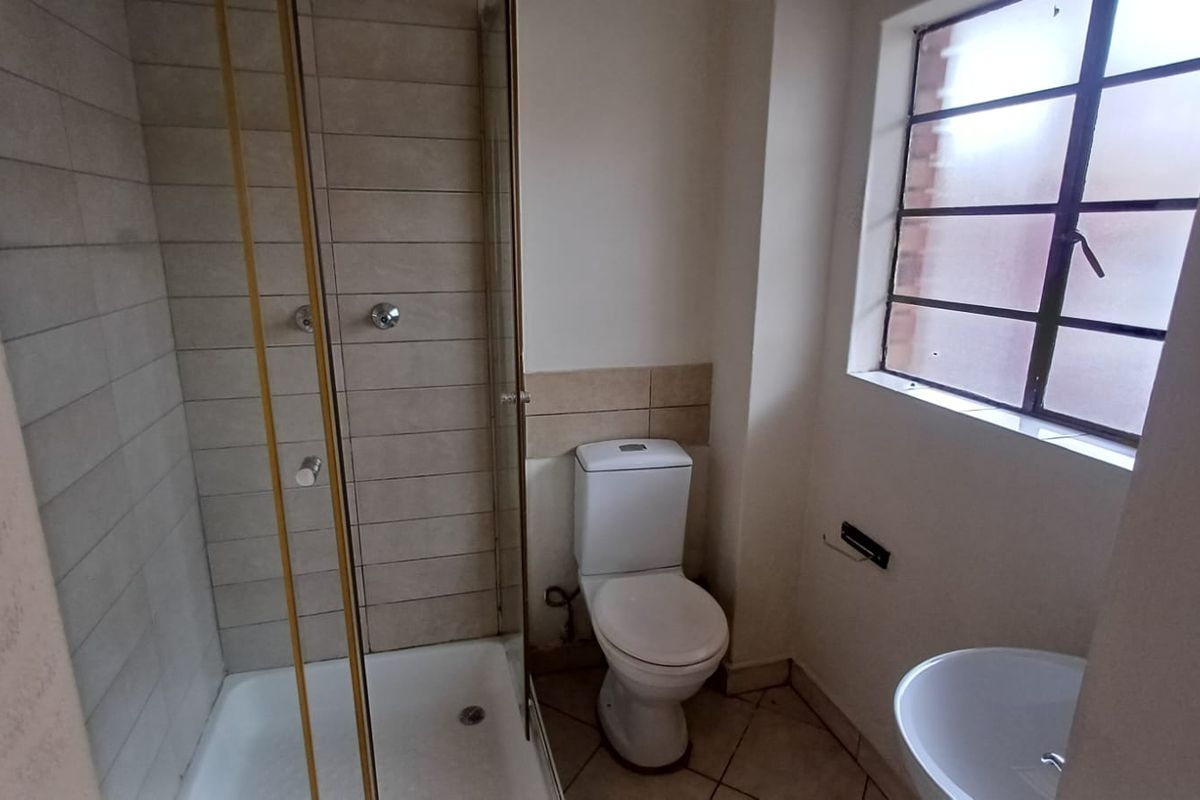 A functional bathroom featuring a shower enclosure, toilet, and washbasin with tiled flooring and wall finishes.