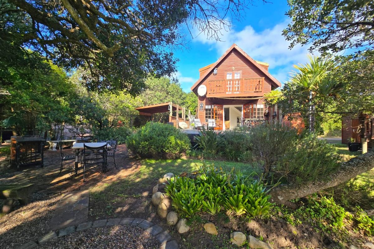 Rear view of a timber-clad house featuring a wooden balcony, deck area, and pergola set within a lush, landscaped garden.