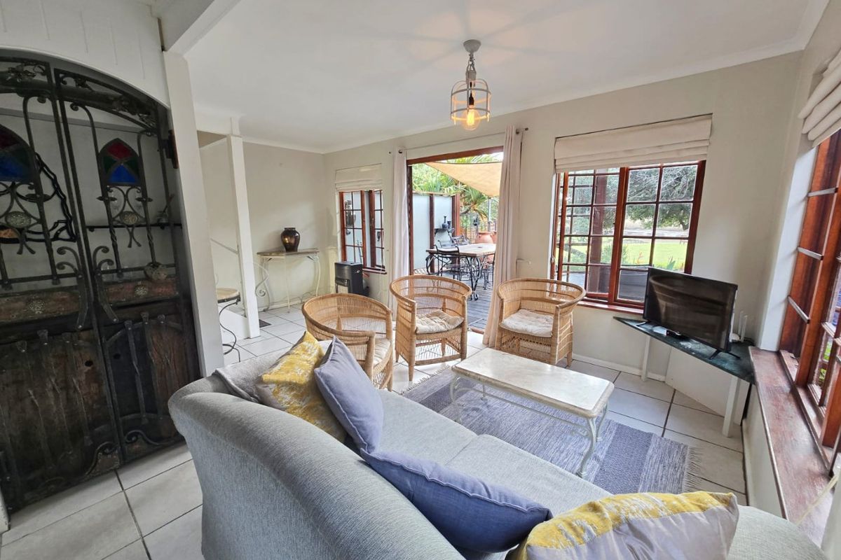 A bright living room featuring tiled floors, timber-framed windows, and a decorative wrought iron security gate, with direct access to an outdoor patio area.