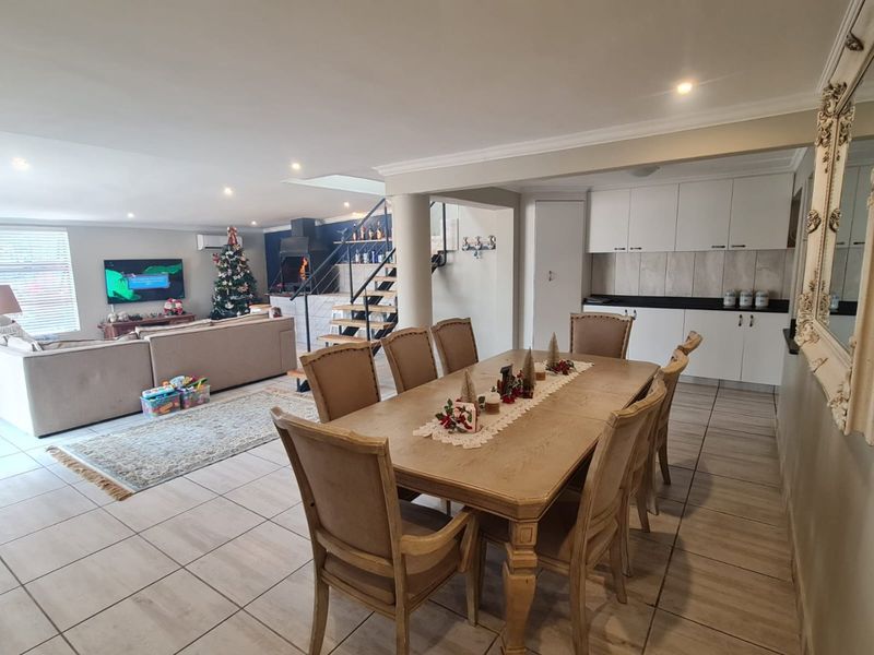 Spacious open-plan living and dining area featuring tiled floors, a modern staircase, a built-in fireplace, and integrated kitchen cabinetry.