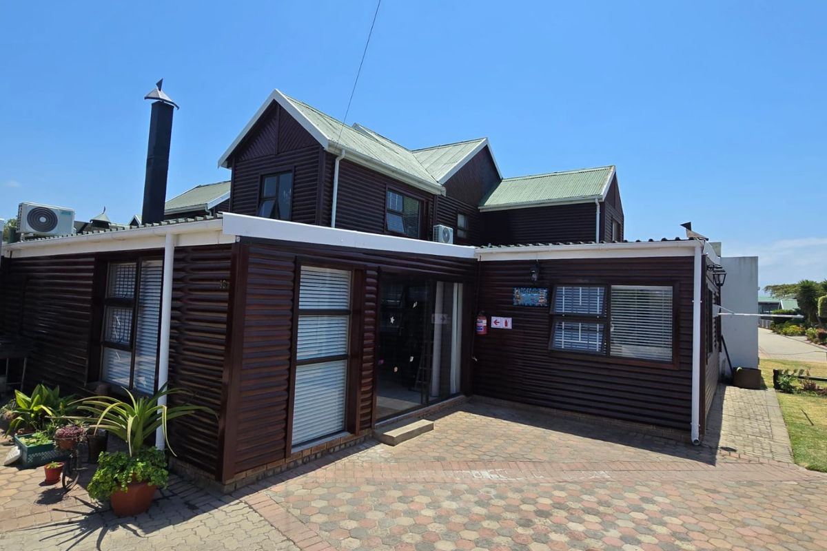 Rear view of a timber-clad house featuring a paved courtyard, external chimney, and sliding glass door access.