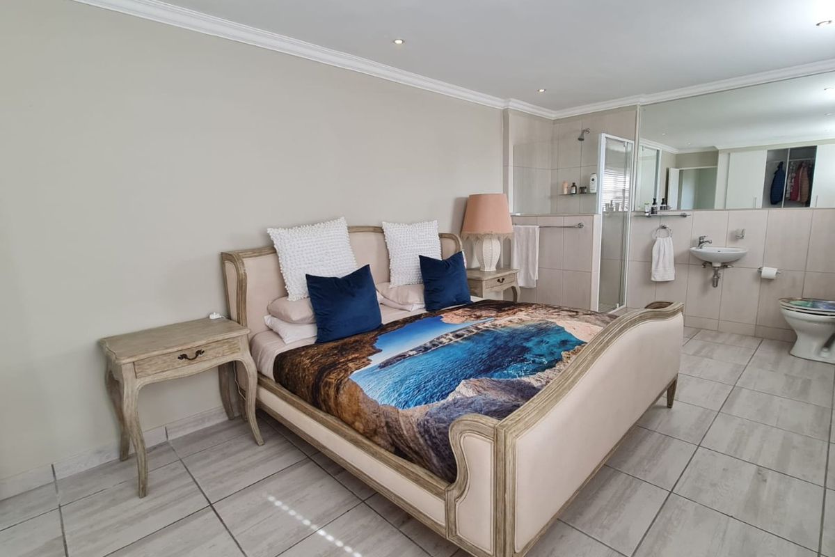 Spacious bedroom featuring tiled flooring, crown molding, and an integrated en-suite bathroom with a glass shower enclosure and wall-mounted basin.