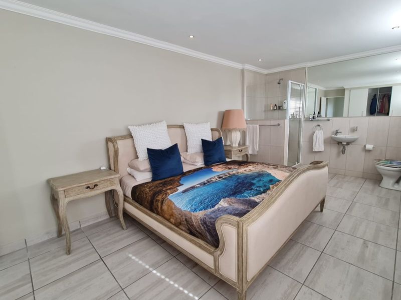 Spacious bedroom featuring tiled flooring, crown molding, and an integrated en-suite bathroom with a glass shower enclosure and wall-mounted basin.