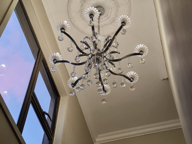 A high-ceilinged hallway area featuring an elegant crystal chandelier, decorative ceiling rose, and classic cornice detailing.