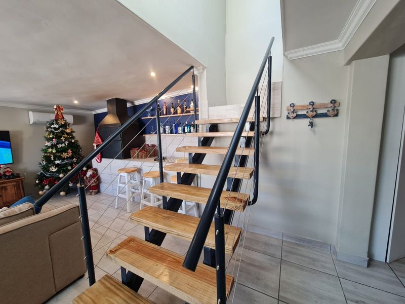 Open-plan living area featuring a modern open-tread staircase with metal railings and a built-in fireplace, finished with neutral floor tiles.
