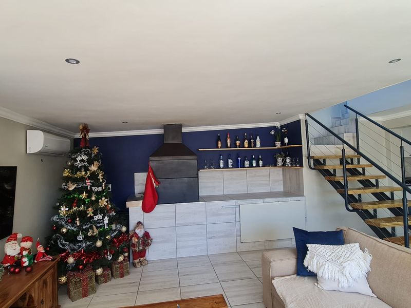 Open plan living area featuring a built-in braai, floating shelving, tiled flooring, and a modern staircase with metal balustrades.