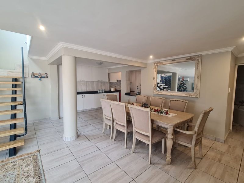 Open plan dining area featuring tiled flooring, a structural column, and an adjacent kitchen with built-in cabinetry and a staircase.