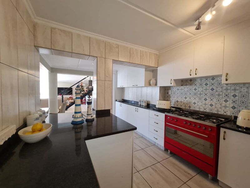 A functional kitchen featuring white cabinetry, dark granite countertops, a decorative tiled backsplash, and a prominent red gas stove.