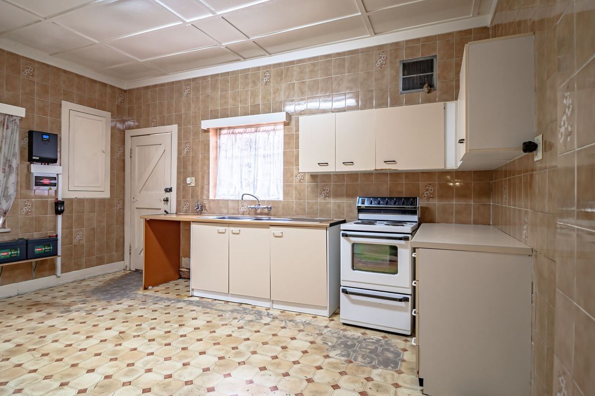 A dated kitchen featuring tiled walls and flooring, built-in cabinetry, a stainless steel sink, and a freestanding stove with an integrated inverter system.