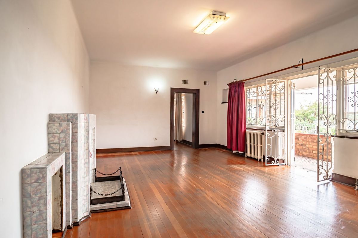 Spacious living room featuring original hardwood flooring, a tiled fireplace, and direct access to an outdoor patio through secure french doors.