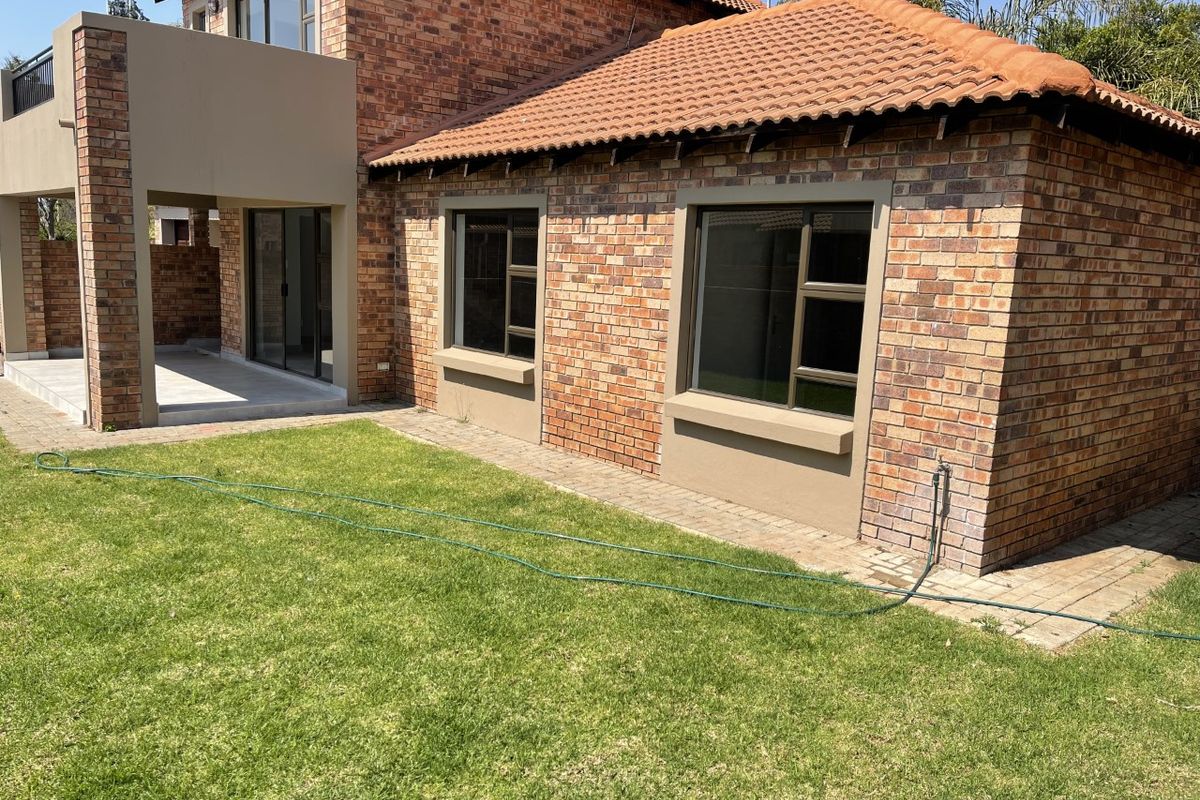 Rear view of the townhouse featuring a face brick facade, terracotta roof tiles, aluminium windows, and a paved patio area overlooking the garden.