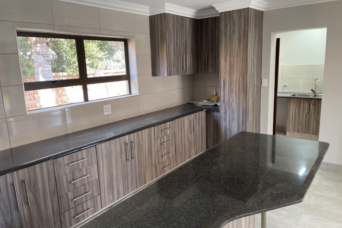 Modern kitchen featuring granite countertops, wood-grain laminate cabinetry, and a functional island, with an adjacent scullery area visible.