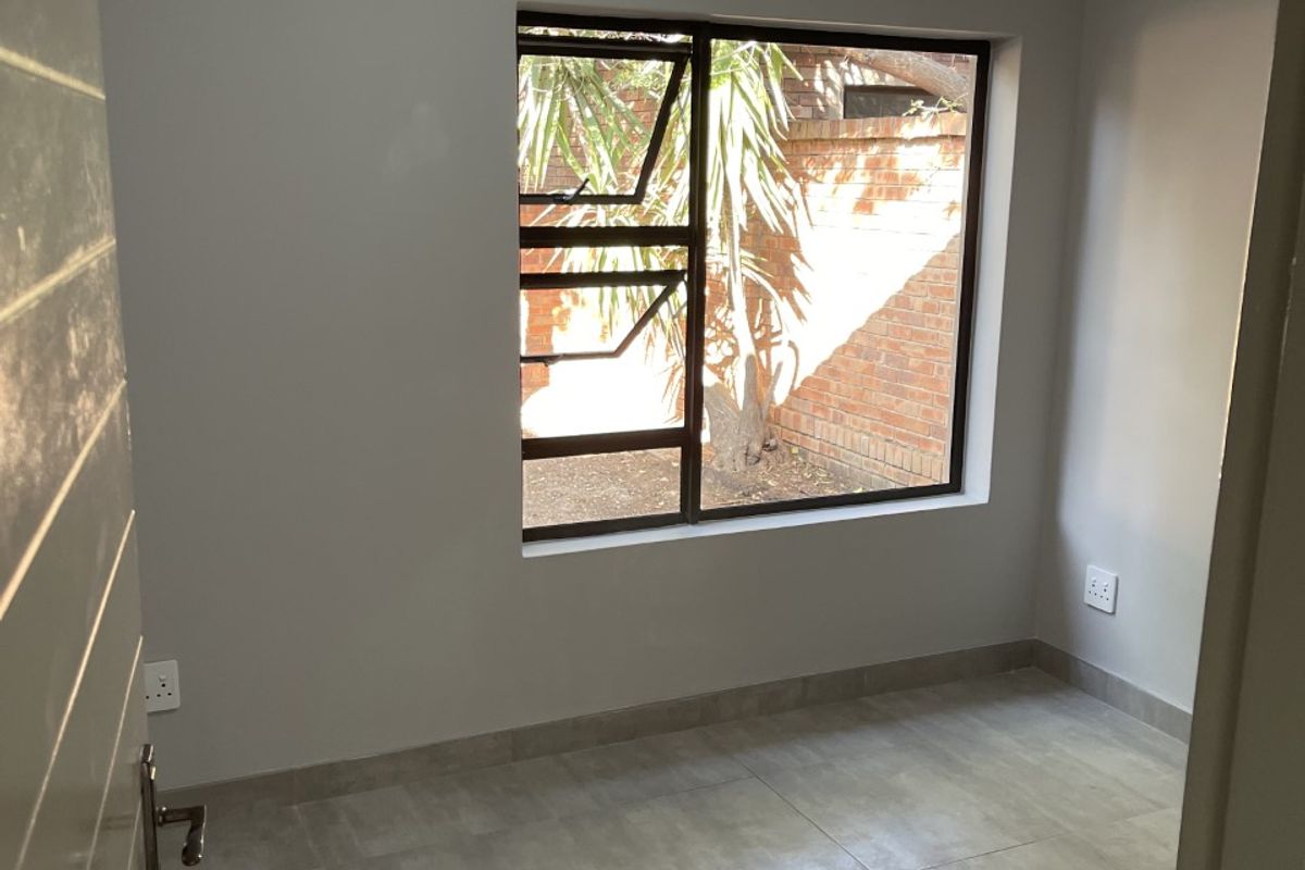 A clean, empty bedroom featuring neutral grey tiled flooring, modern aluminium window frames, and crisp wall finishes, ready for personalization.