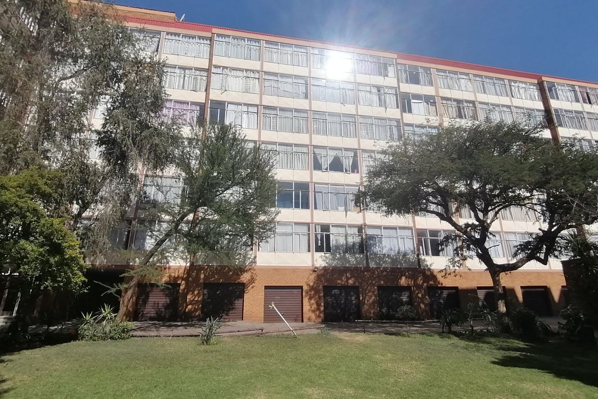 Exterior view of a multi-story apartment building featuring a brick ground floor with garage access and a large landscaped lawn area.