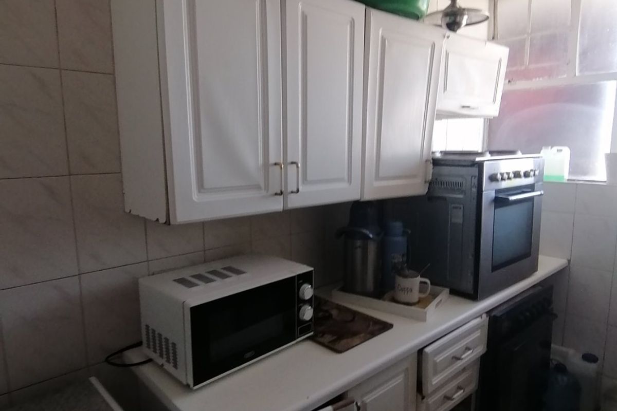 A compact kitchen featuring white cabinetry, tiled backsplash, and tiled flooring. The space shows signs of wear and requires maintenance or cosmetic updates.