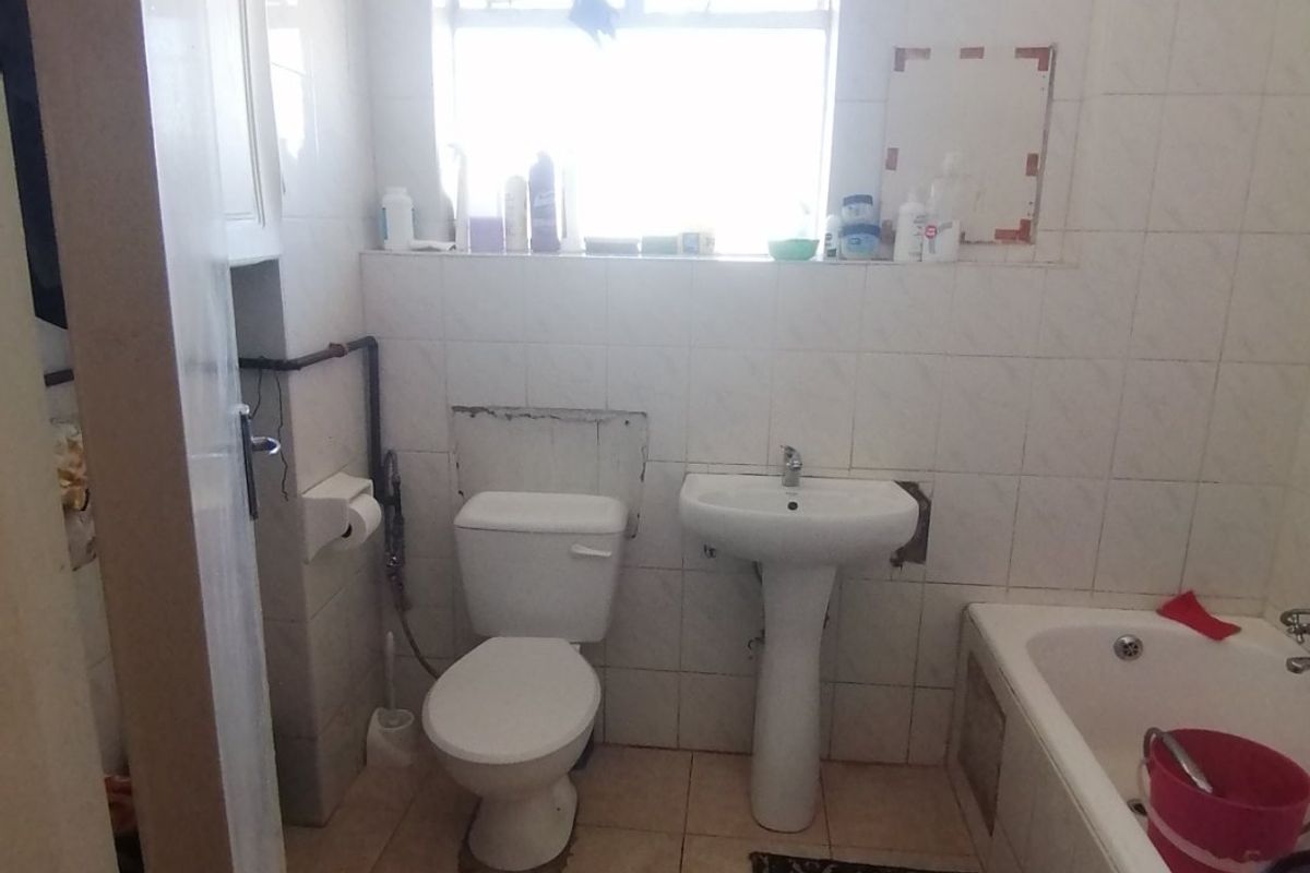 A dated bathroom featuring a pedestal basin, toilet, and bathtub with tiled finishes, currently requiring maintenance and cosmetic updates.