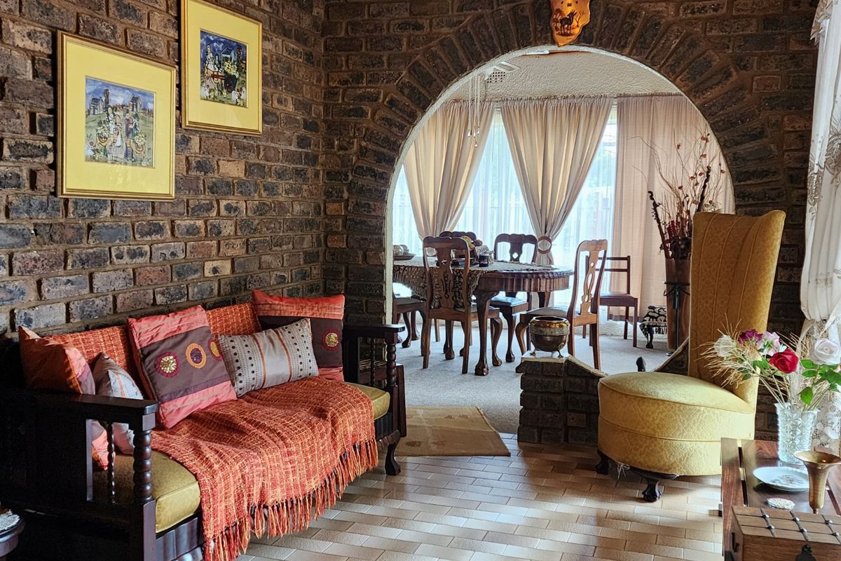 A living room featuring a distinctive exposed brick wall and a large brick archway leading into an adjacent dining area with tiled flooring.