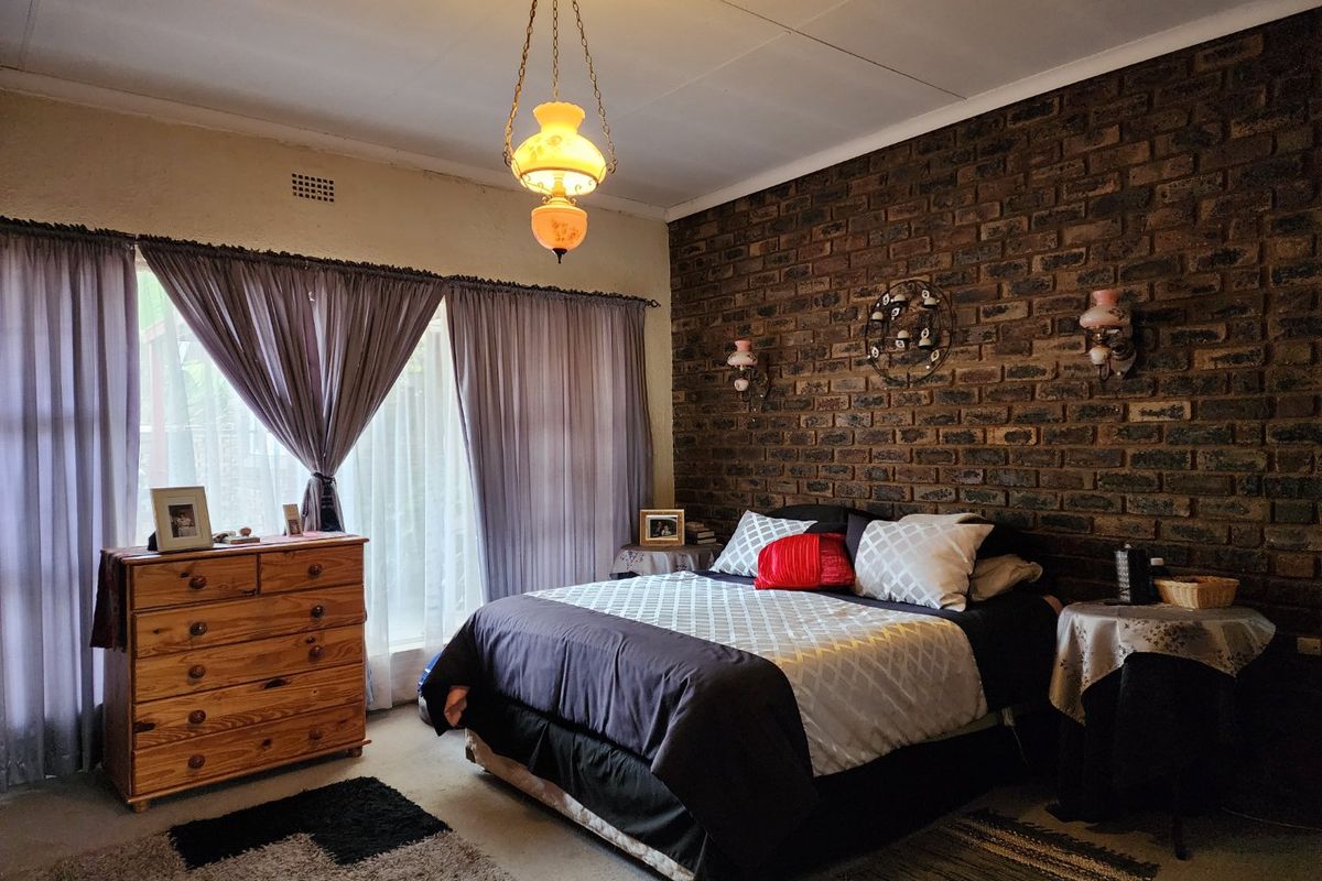A bedroom featuring an exposed brick feature wall, pendant lighting, and wall-mounted sconces, offering a rustic aesthetic with potential for modern updates.