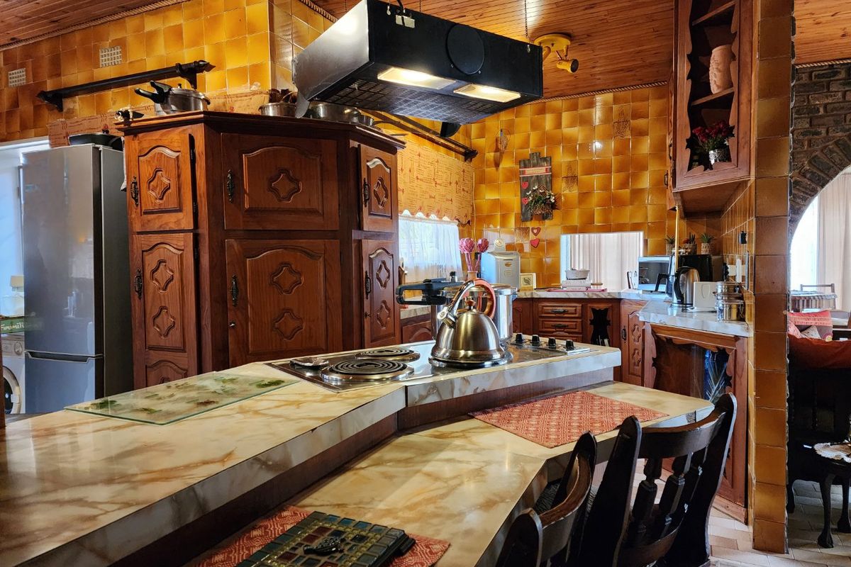 A traditional kitchen featuring extensive wooden cabinetry, marble-effect countertops, an integrated hob with extractor fan, and distinctive amber-toned wall tiling.