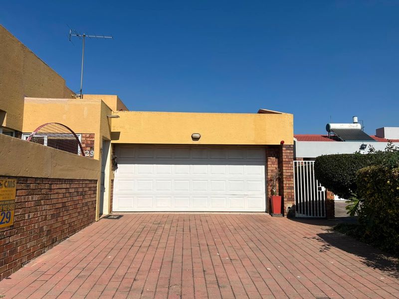 Front exterior view featuring a paved driveway, single sectional garage door, and brick boundary wall with integrated security gate.