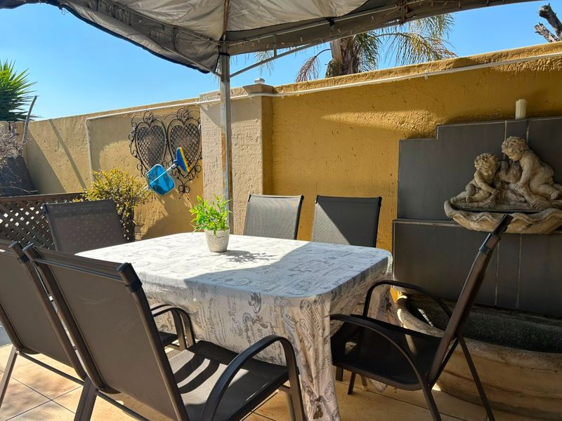 A covered outdoor patio area featuring tiled flooring, a boundary wall, and a built-in water feature, providing a functional space for outdoor dining.