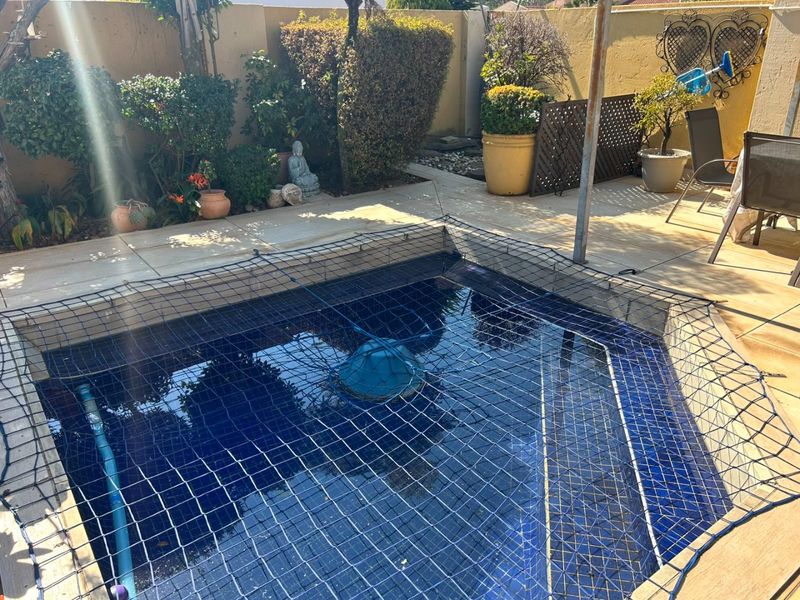 A compact swimming pool area featuring a safety net, tiled surround, and perimeter boundary wall, suitable for outdoor relaxation.