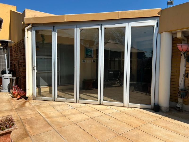 A covered patio area featuring large aluminium stacker doors, tiled flooring, and a structural brick pillar, providing seamless indoor-outdoor flow.