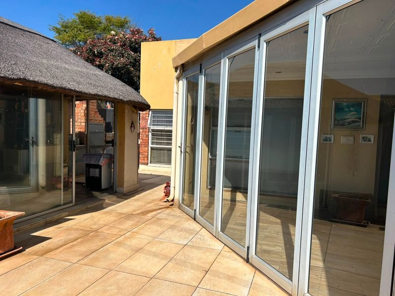 Outdoor patio area featuring tiled flooring, aluminium stacker doors, and a covered thatched section with a built-in braai facility.