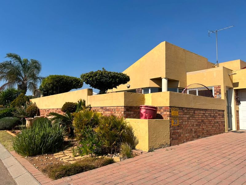 Front elevation of a house featuring a brick and stucco boundary wall, paved driveway, and established garden landscaping.