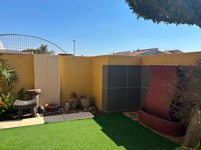 A compact private garden area featuring artificial turf, a tiled patio section, and a boundary wall with integrated decorative tiling.