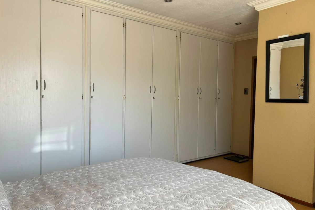 A bedroom featuring extensive built-in cupboards, recessed downlighting, and laminate flooring, offering ample storage space.