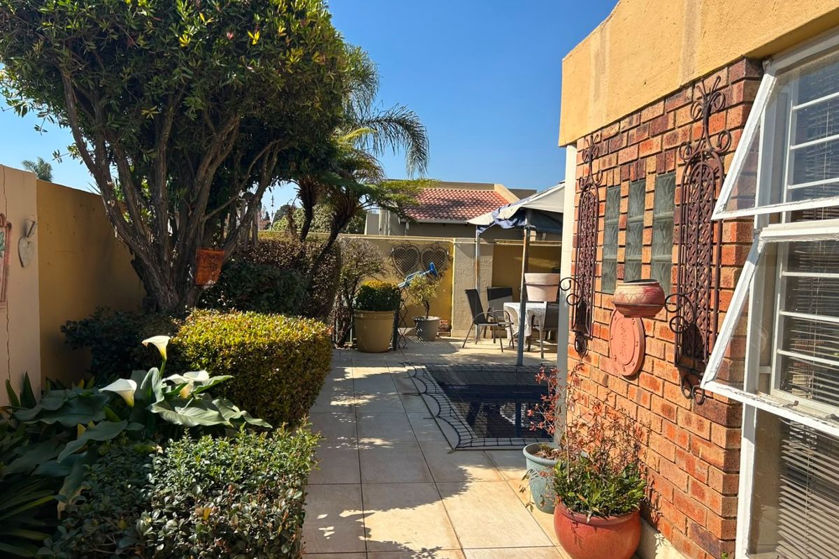 A well-maintained rear garden area featuring a paved patio, established landscaping, and a brick exterior wall with decorative metal accents.
