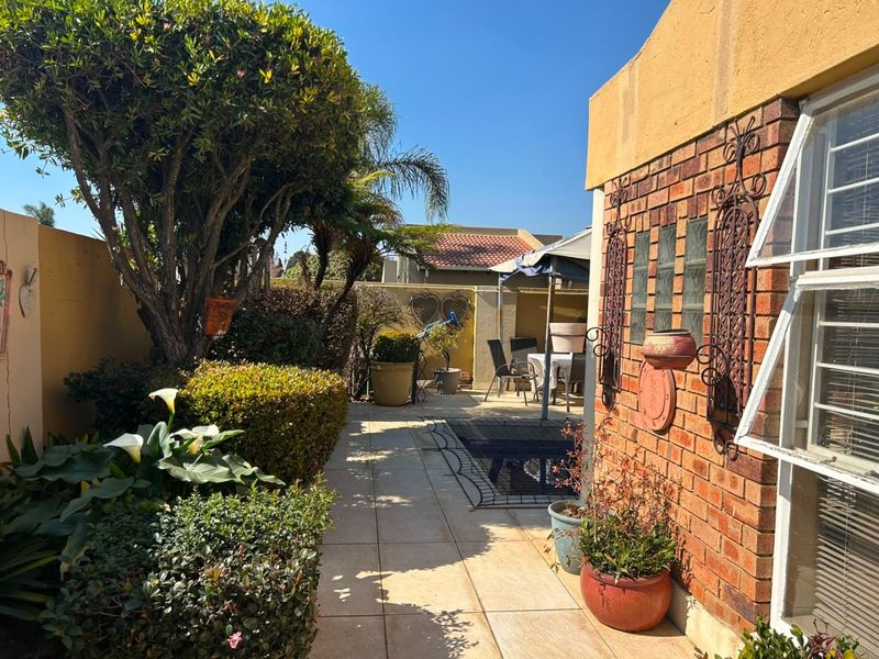 A well-maintained rear garden area featuring a paved patio, established landscaping, and a brick exterior wall with decorative metal accents.