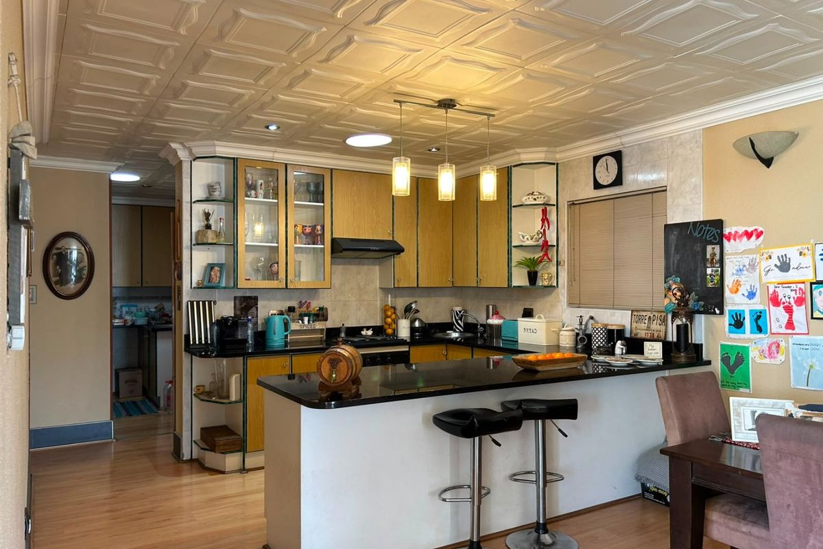 A functional kitchen featuring laminate cabinetry, granite countertops, a breakfast bar, and a distinctive coffered ceiling, with an adjacent scullery area.