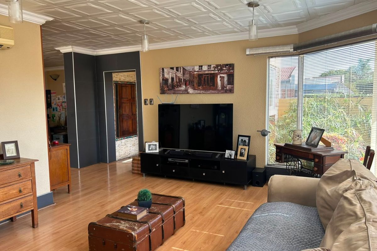 Spacious living room featuring laminate flooring, a distinctive coffered ceiling, and a large bay window that provides ample natural light.