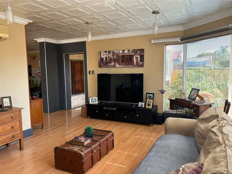 Spacious living room featuring laminate flooring, a distinctive coffered ceiling, and a large bay window that provides ample natural light.