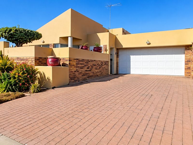 Front view of a well-maintained house featuring a paved driveway, double garage, and established garden landscaping.
