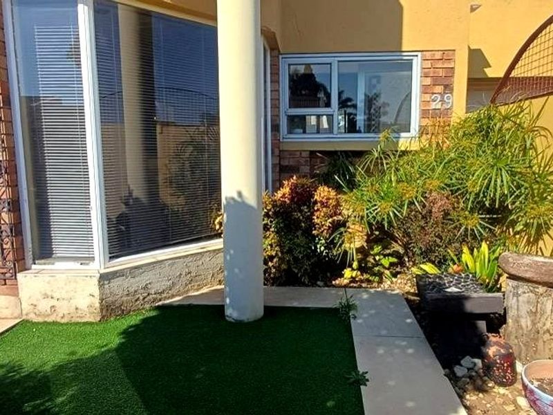 A rear exterior view featuring a small artificial lawn, paved walkway, and brick facade with large windows.