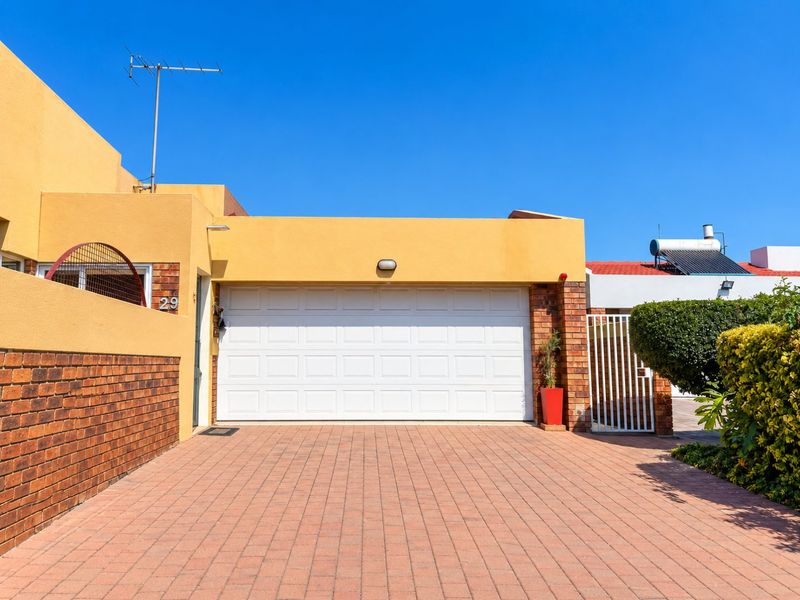 Front view of the property featuring a paved driveway, a white sectional garage door, and a well-maintained brick and rendered facade.