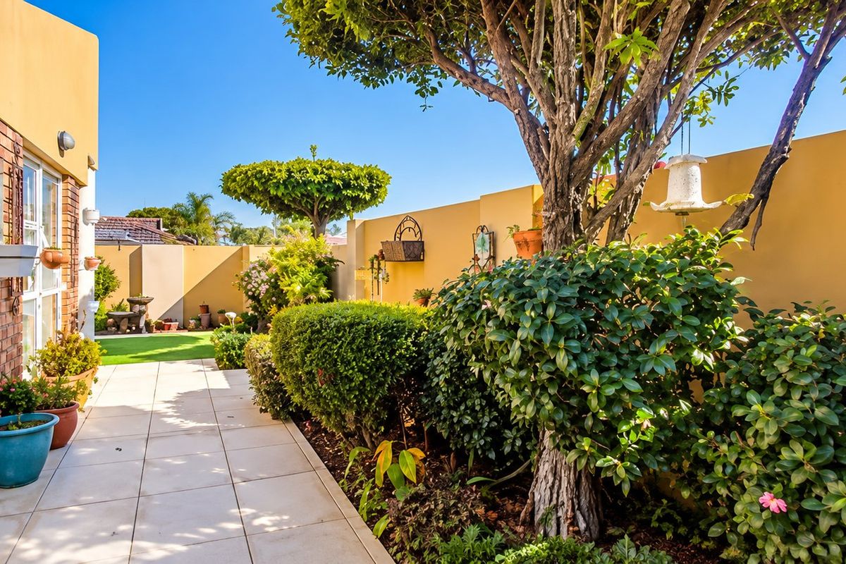 A well-maintained rear garden area featuring a tiled patio, established landscaping, and a solid boundary wall, providing a private outdoor space.