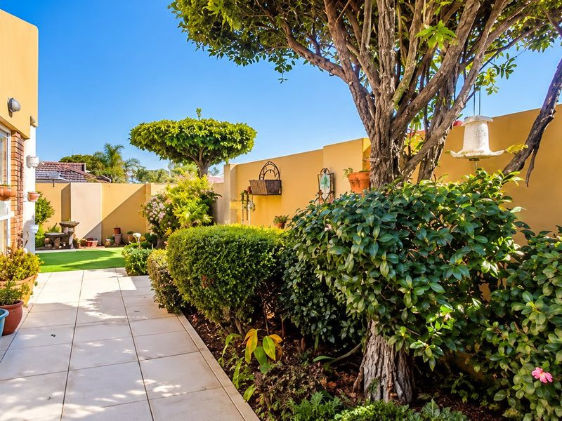 A well-maintained rear garden area featuring a tiled patio, established landscaping, and a solid boundary wall, providing a private outdoor space.