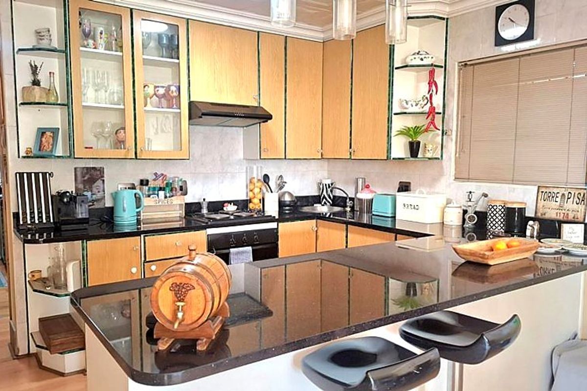 A functional kitchen featuring light wood-tone cabinetry, dark granite countertops, integrated appliances, and a breakfast bar peninsula.